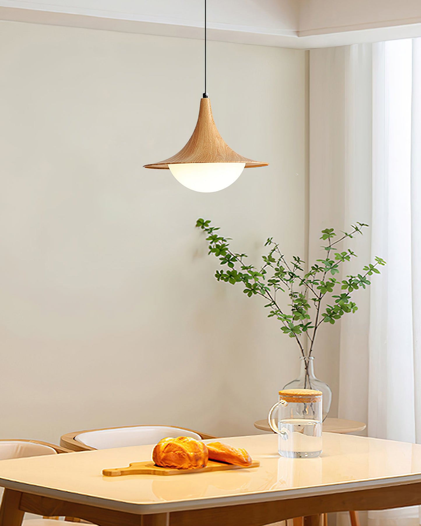 Dining area with a wooden pendant light, table, and vase with greenery.