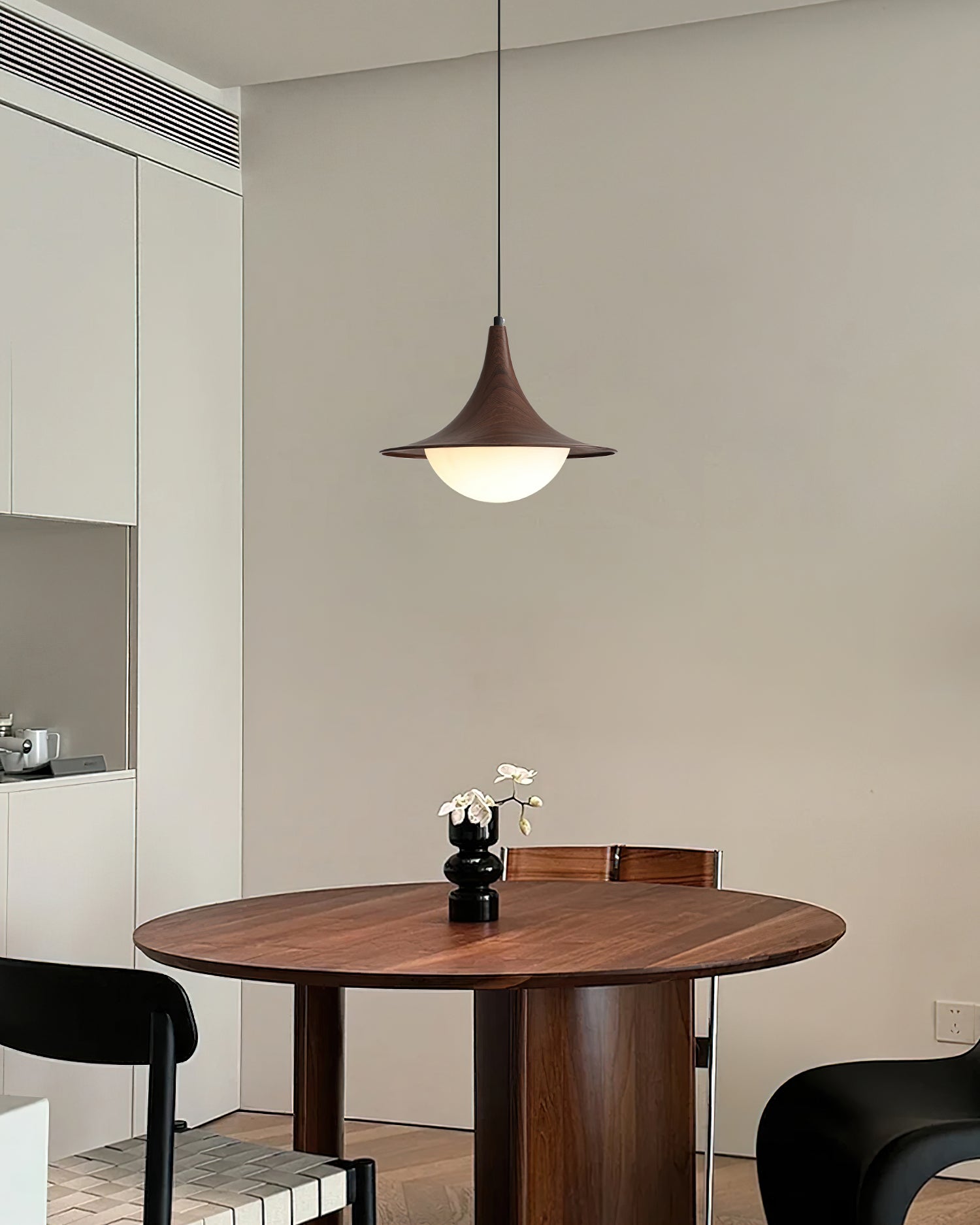 Wooden dining table with a pendant light and black chairs in a modern kitchen.