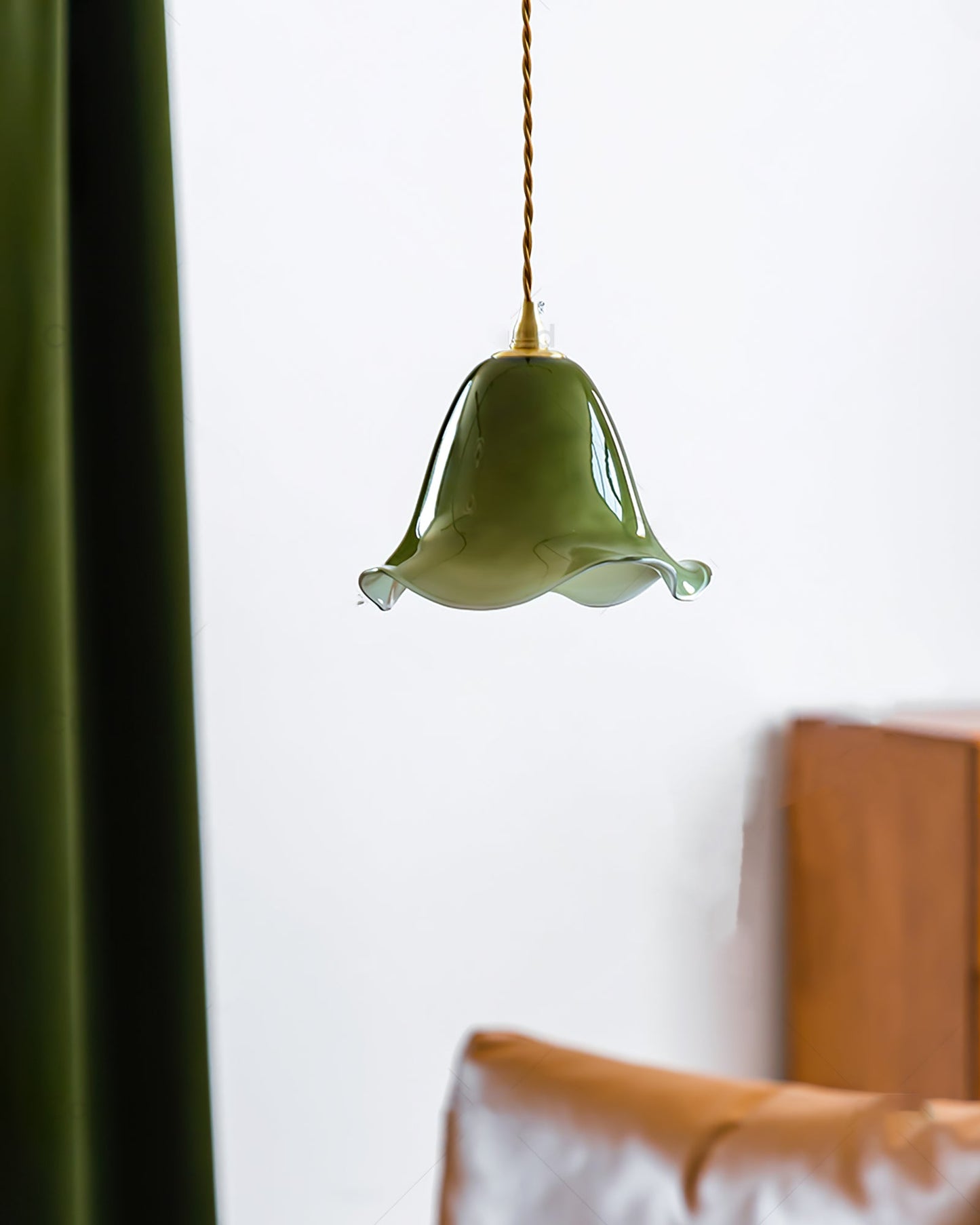 Green pendant light hanging against a white wall with a wooden headboard.