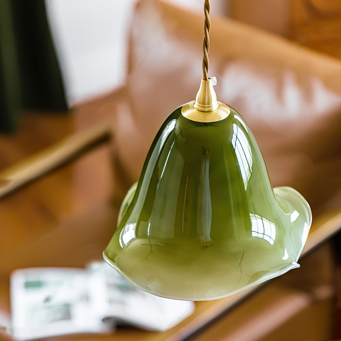 Green glass pendant light with gold fixture on a blurred background