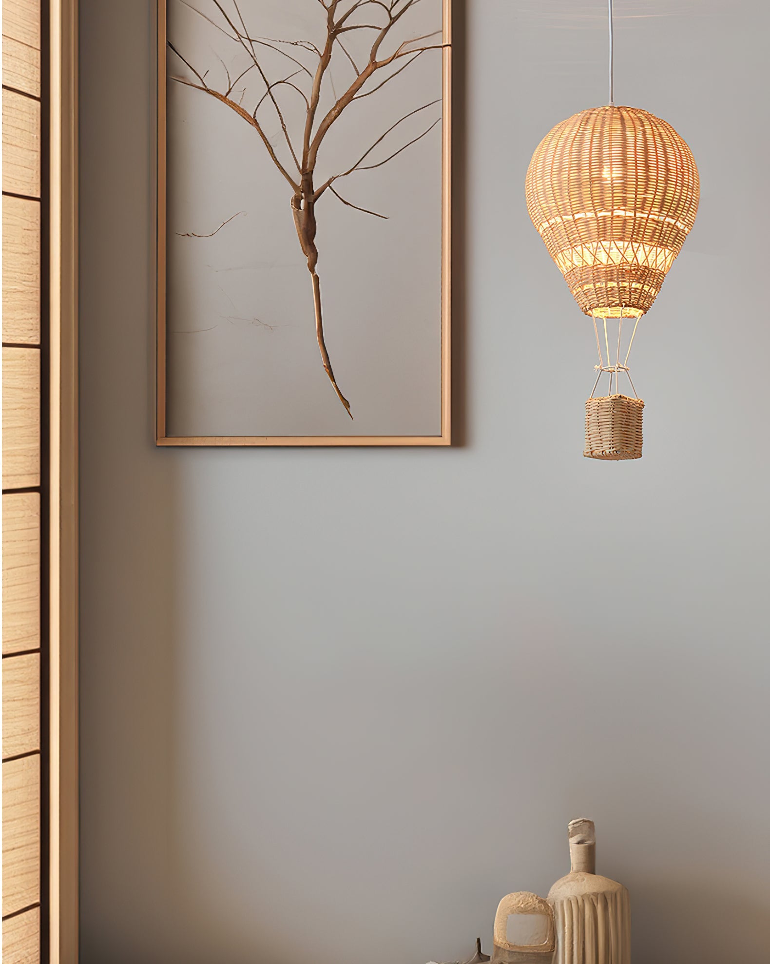 Woven lamp hanging on a wall with a framed picture of a tree.