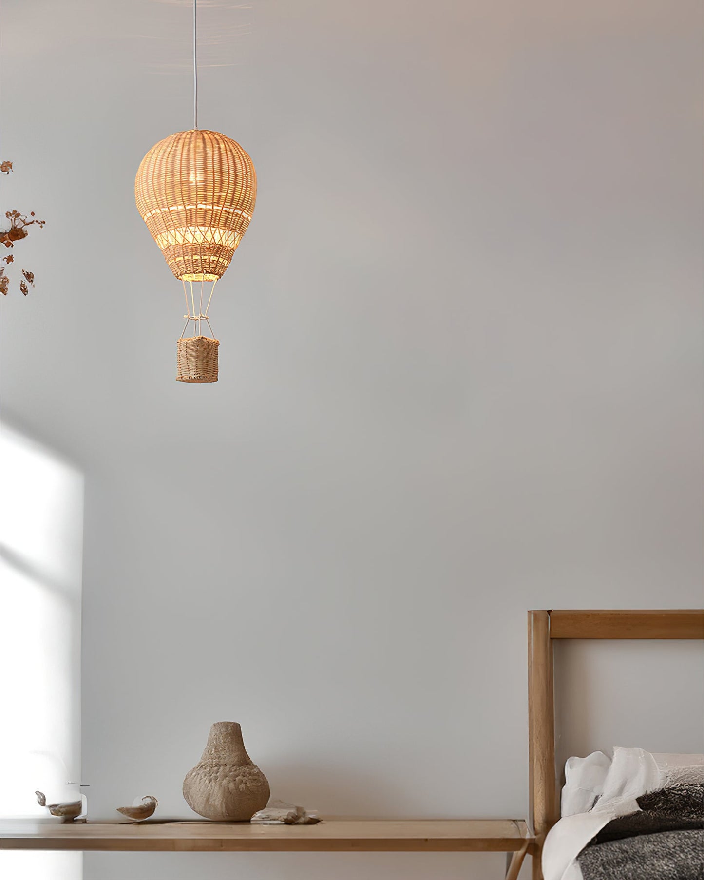 Woven pendant light hanging above a wooden shelf with decorative items against a plain wall.