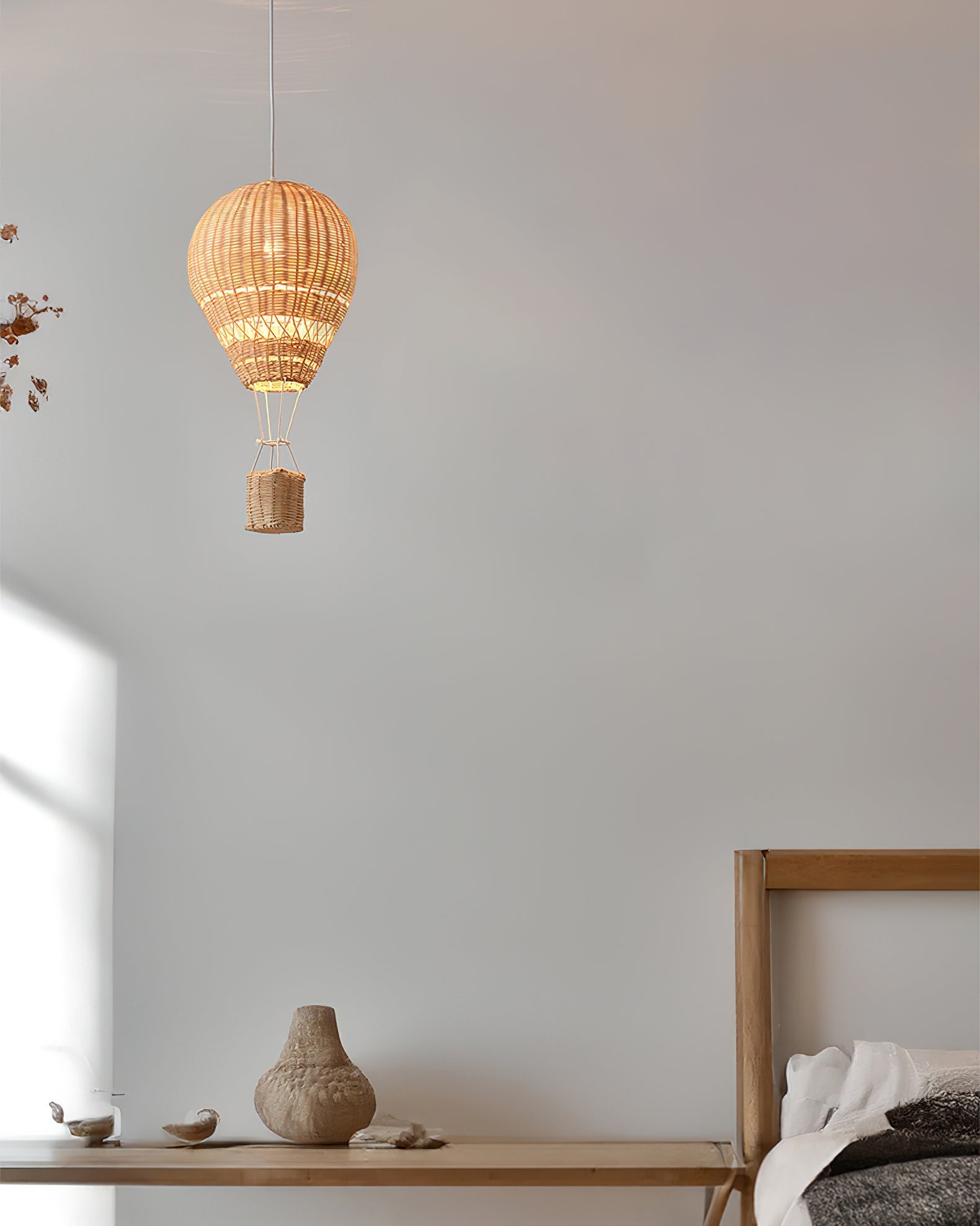 Woven pendant light hanging above a wooden shelf with decorative items against a plain wall.
