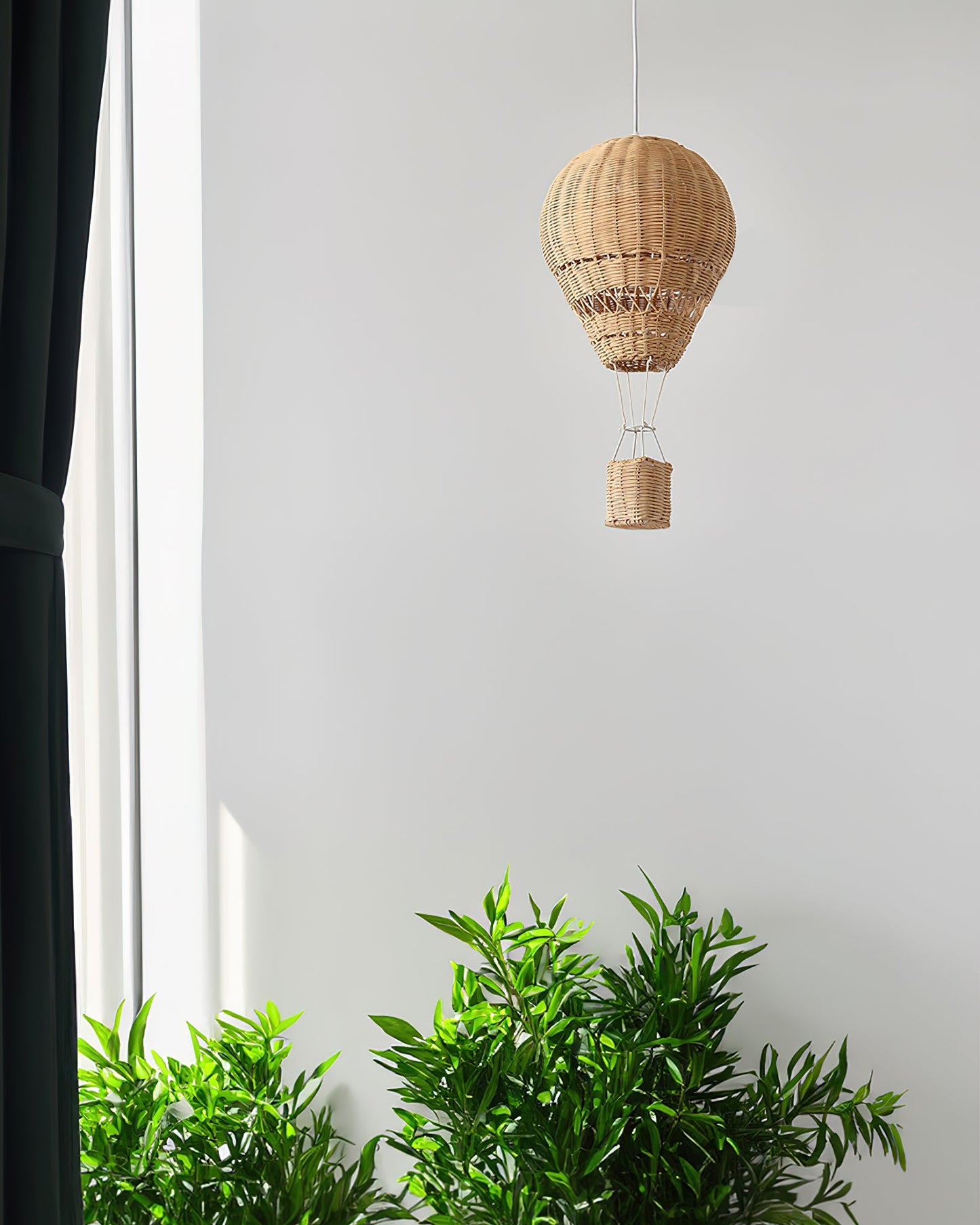 Woven hot air balloon decoration hanging against a white wall with green plants at the bottom.