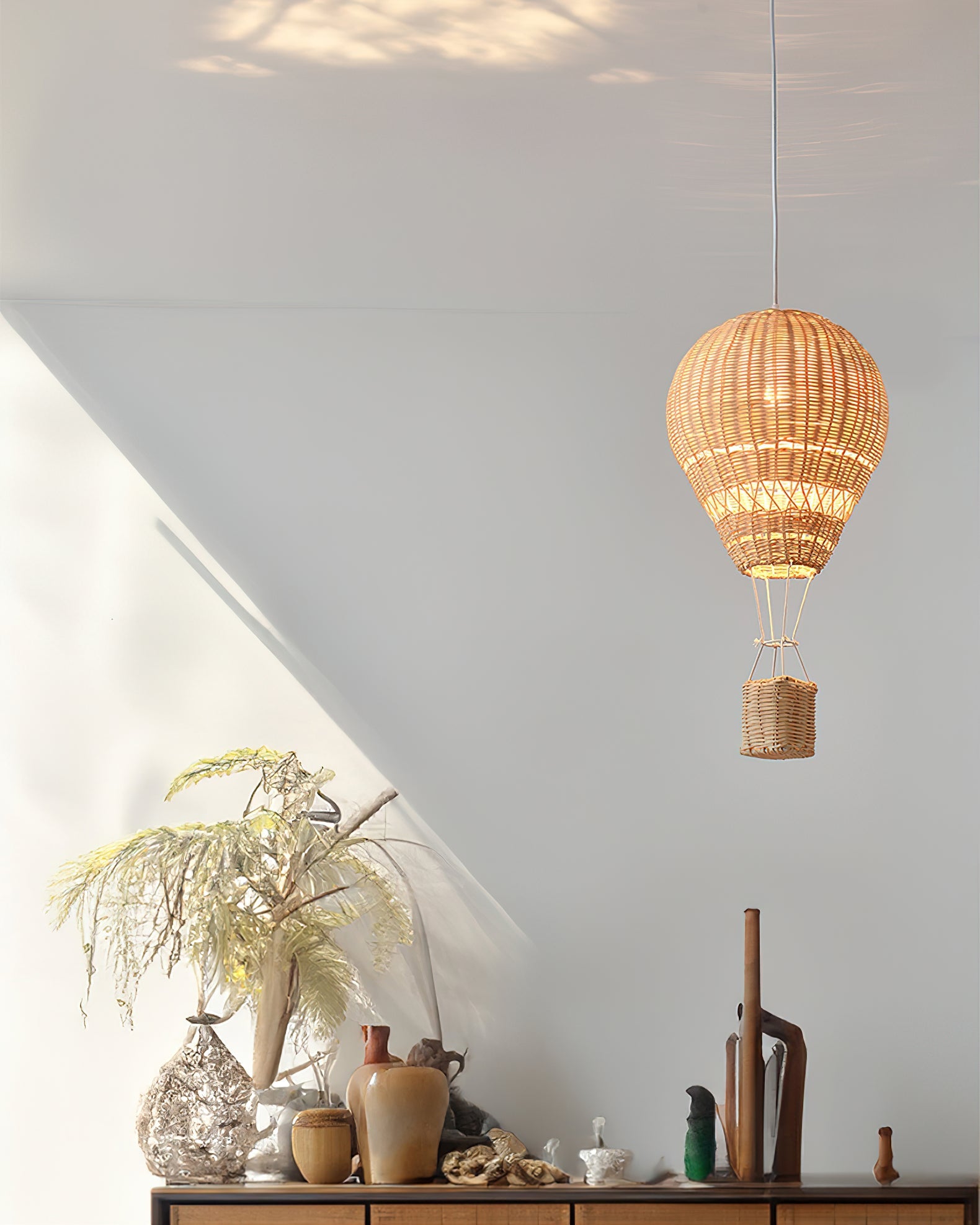 Woven lamp hanging above a table with decorative items against a light gray wall.