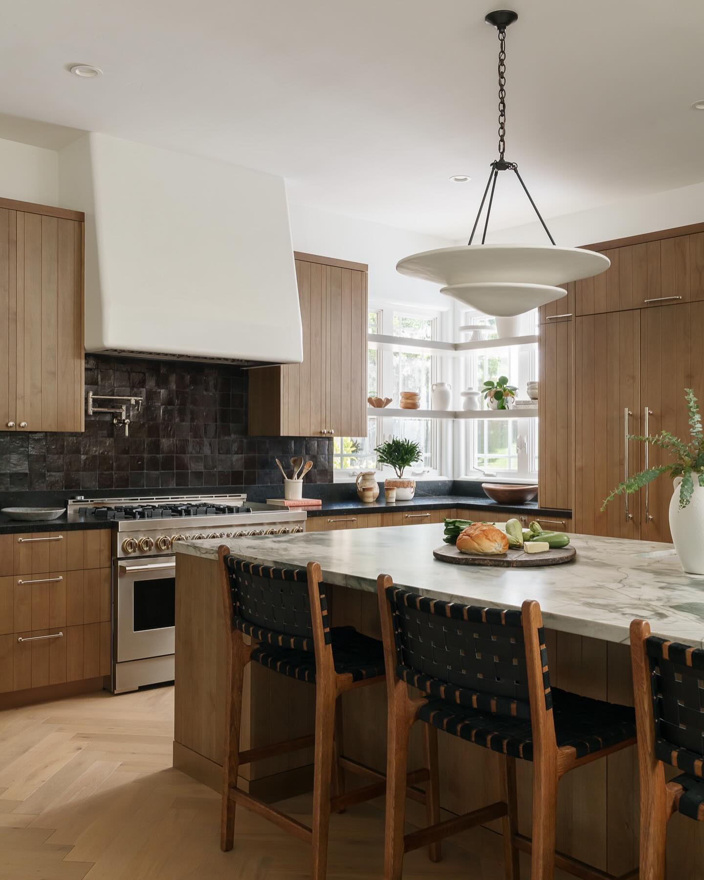 Modern kitchen with wooden cabinets, marble island, and black backsplash.