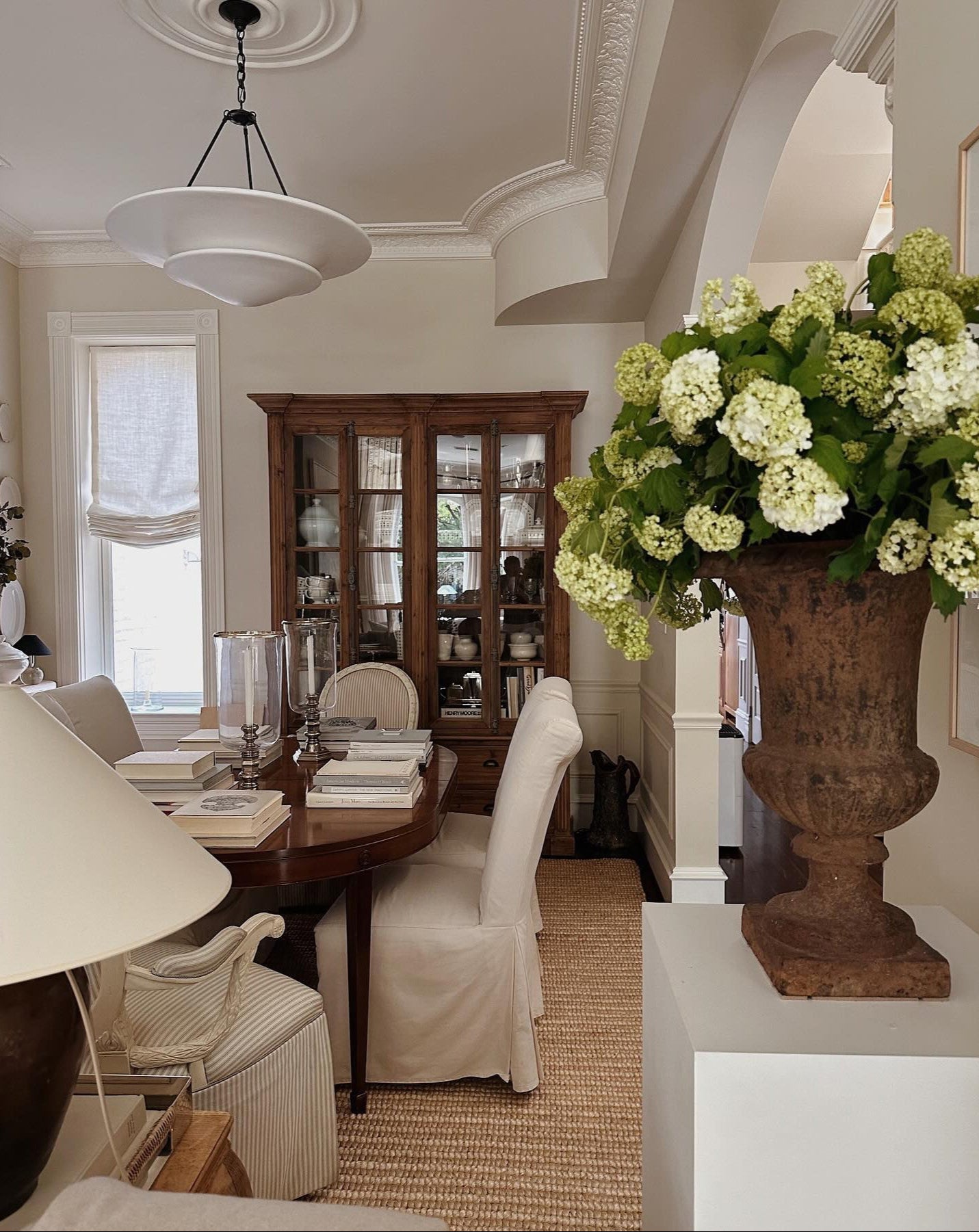 Dining room with a wooden table, chairs, and a large vase of flowers.