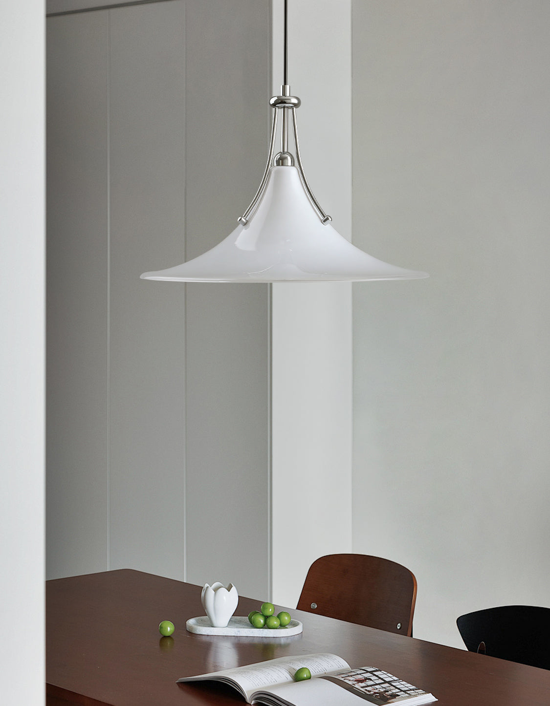 White pendant light hanging above a dining table with a magazine and apples on it.