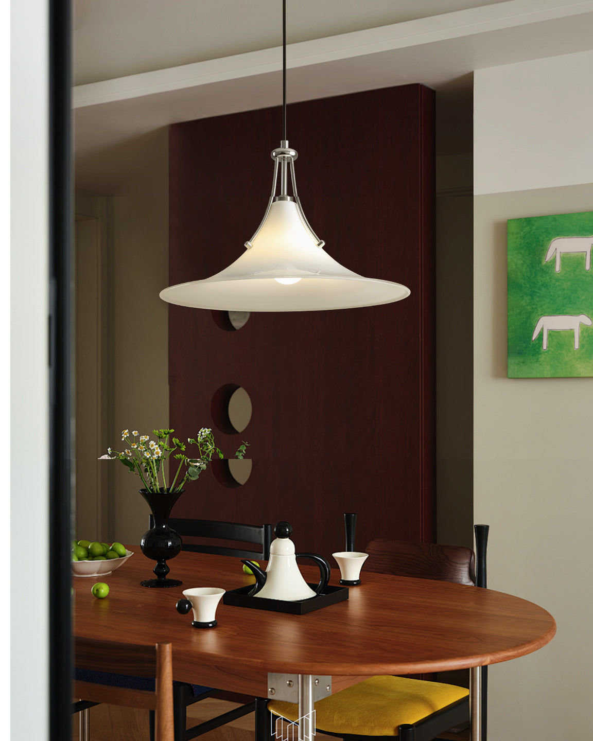 Pendant light fixture hanging above a dining table with a vase and flowers on a dark wall.