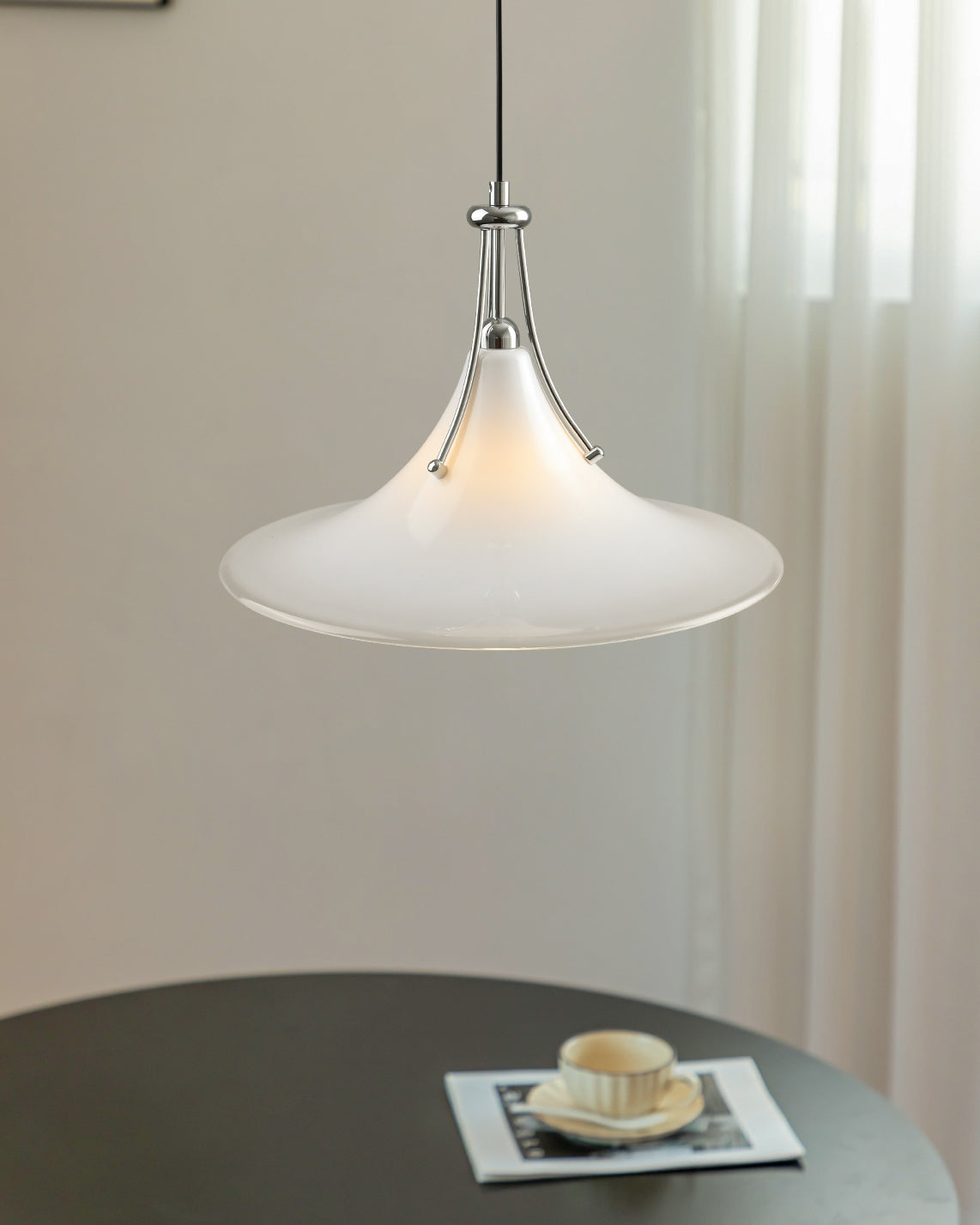Pendant light hanging above a table with a magazine and cup on a neutral background